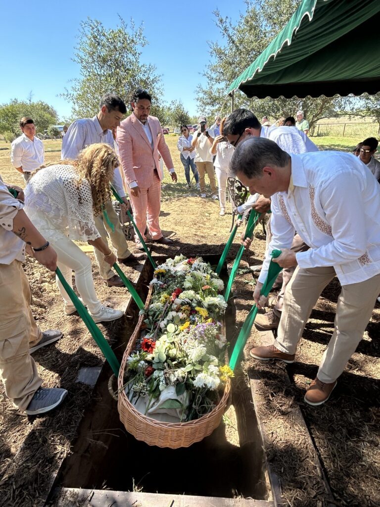 Mourners lowering a wicker casket covered in white flowers into a grave
