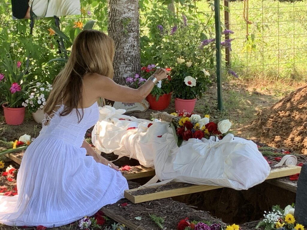 A young woman in a white dress arranging flowers beside a shrouded burial