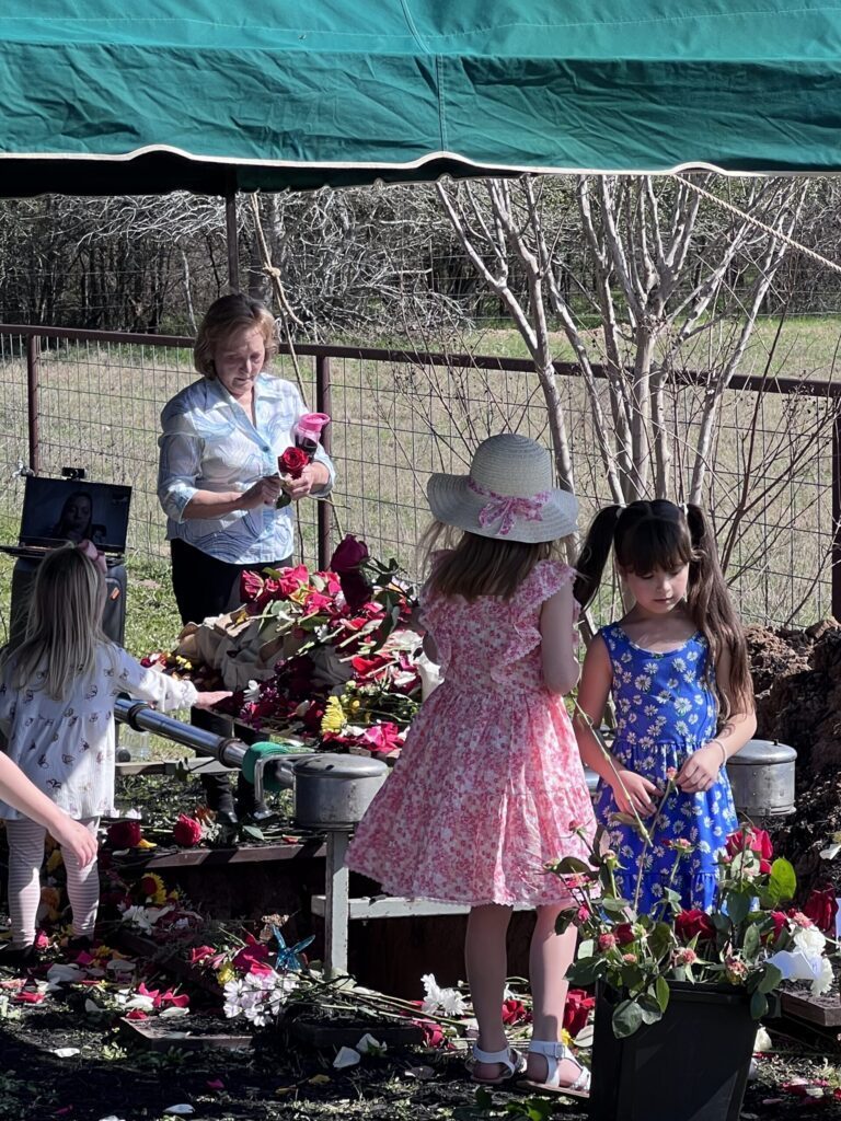 A woman and two young girls placing flowers around a graveside under a canopy