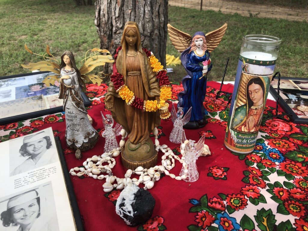 A remembrance altar with religious figurines, a candle, photographs, and red flowers
