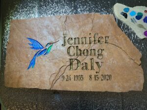 A carved natural stone grave marker with a blue hummingbird design