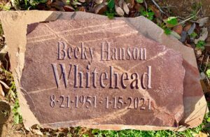 A reddish-brown natural stone grave marker with carved lettering