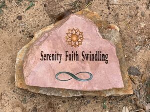 A pink natural stone grave marker with a sunflower and infinity symbol design